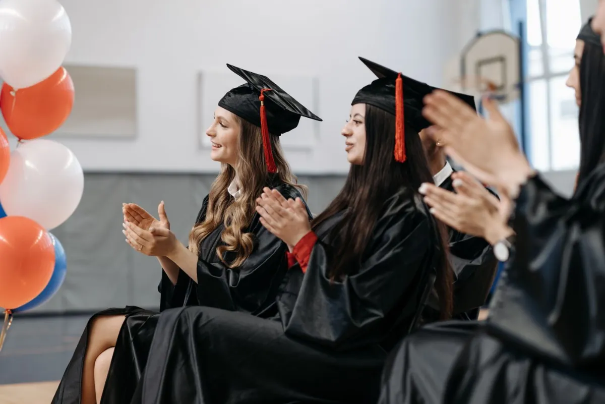 Graduates in caps and gowns applauding at a ceremony