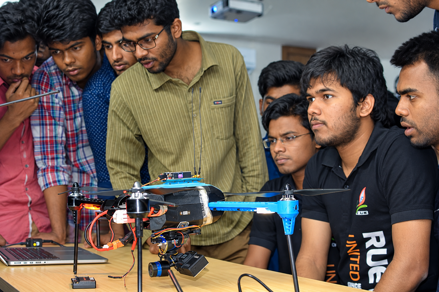 Students gathered around a drone on a workshop table, watching a demonstration