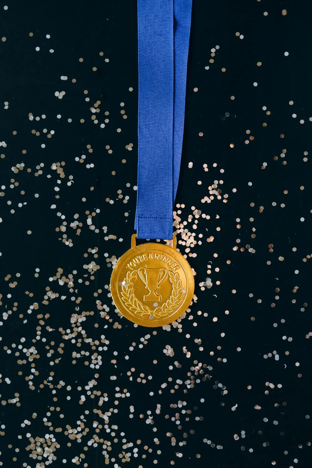 A gold medal on a dark surface scattered with confetti